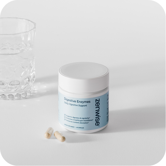 White jar of Zenwise Digestive Enzymes supplement with blue label next to scattered capsules and crystal glass on white surface